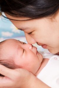 An asian mother kissing her sleeping baby boy